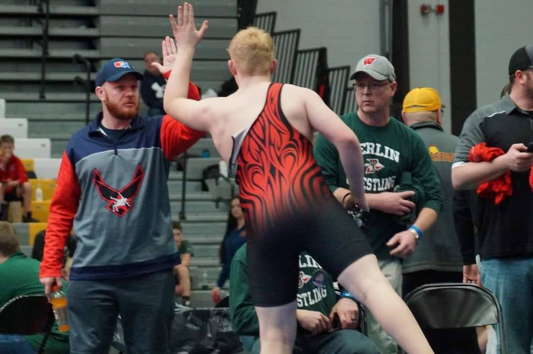 Jason Kleinschmidt coaching an Aviators wrestler beside the competition mat